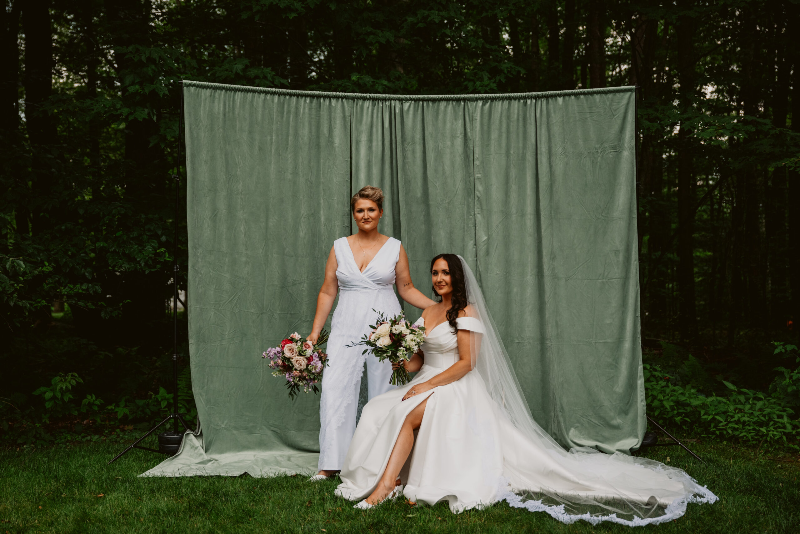 Bride and bride pose in front of green backdrop on wedding day
